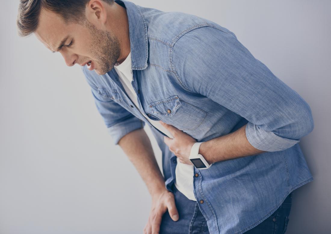 Man with gastritis leaning over and holding his stomach in pain.