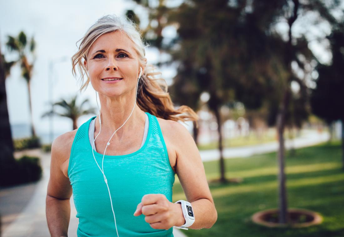 Woman jogging through park listening to headphones.